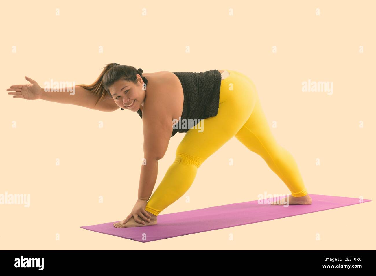 Studio shot of young happy fat Asian woman smiling while bending her back and stretching legs Stock Photo