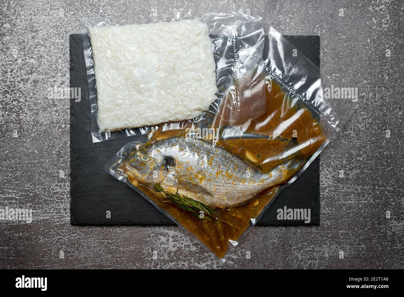 Products in vacuum packaging on black slate board. Fish and rice