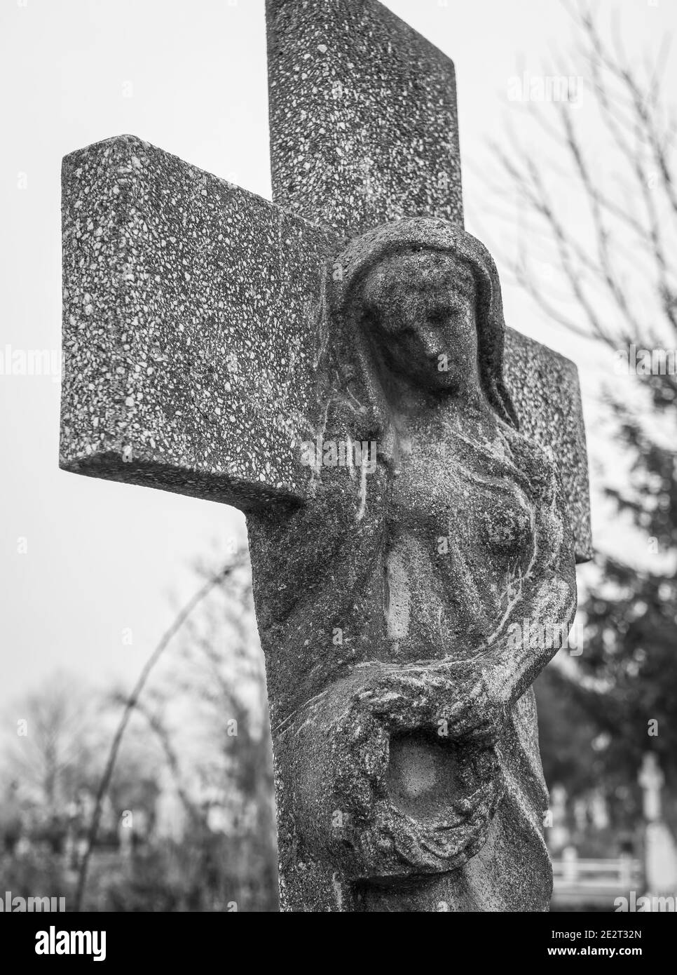 Virgin Mary mourning carved in a stone cross. Stone statue in a cemetery. Stock Photo