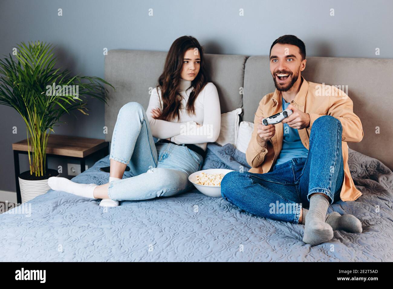 Sweet couple has quarantine free time play video games. She doesn't like  and disappointed felling bored while he is having fun playing with pop corn  b Stock Photo - Alamy