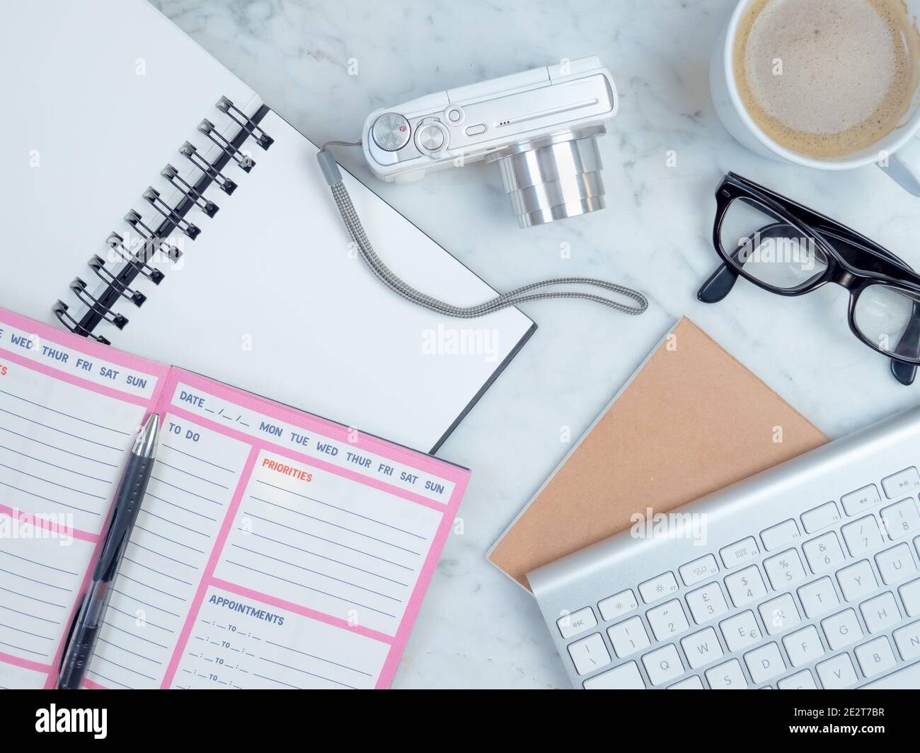 White workplace top view. Notebook and camera on the table. On the desktop are, planner, keyboard, coffee,  glasses. Modern work or study postation.cr Stock Photo
