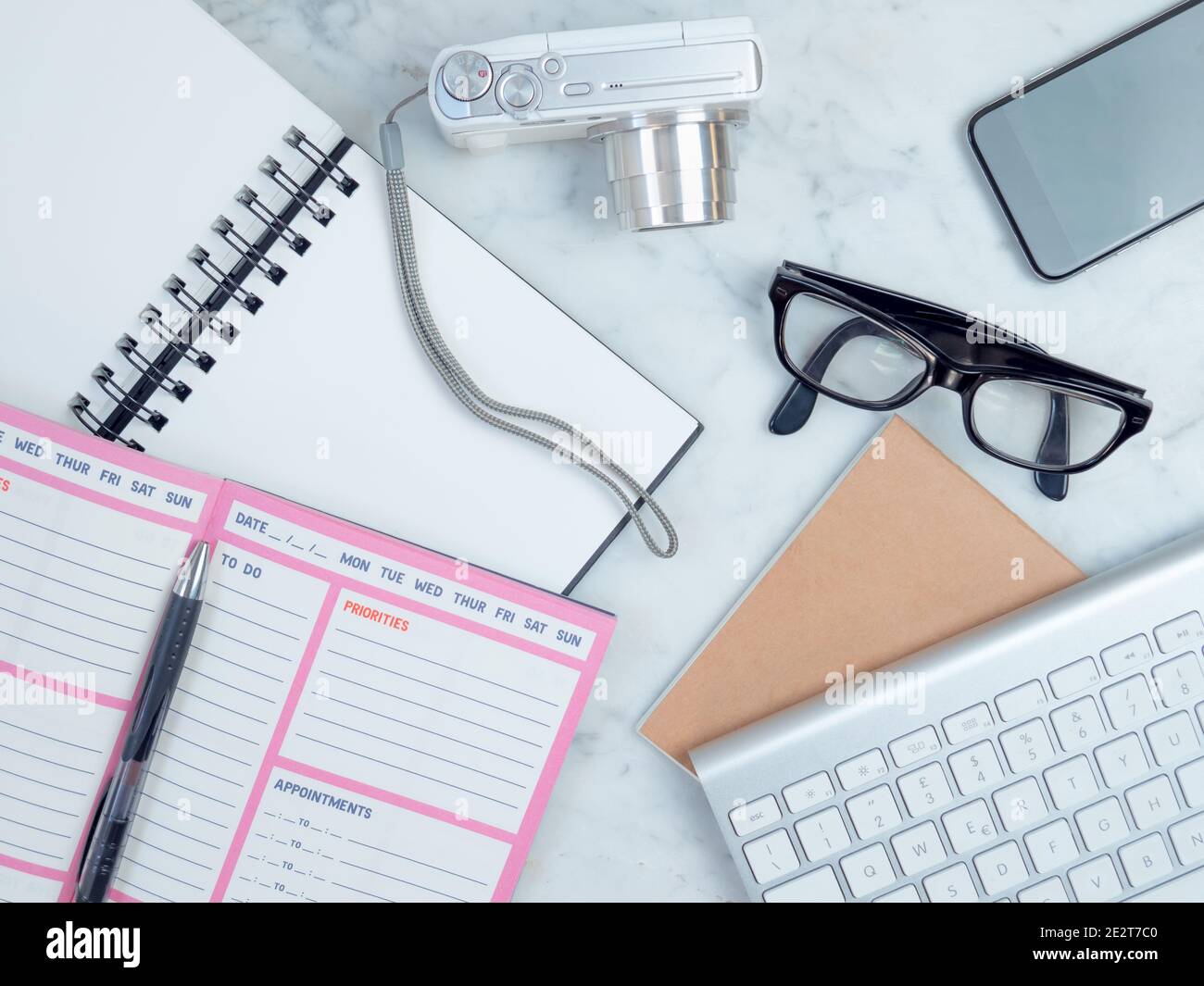 White workplace top view. Notebook and camera on the table. On the desktop are, planner, keyboard, phone, glasses. Modern work or study postation.crea Stock Photo