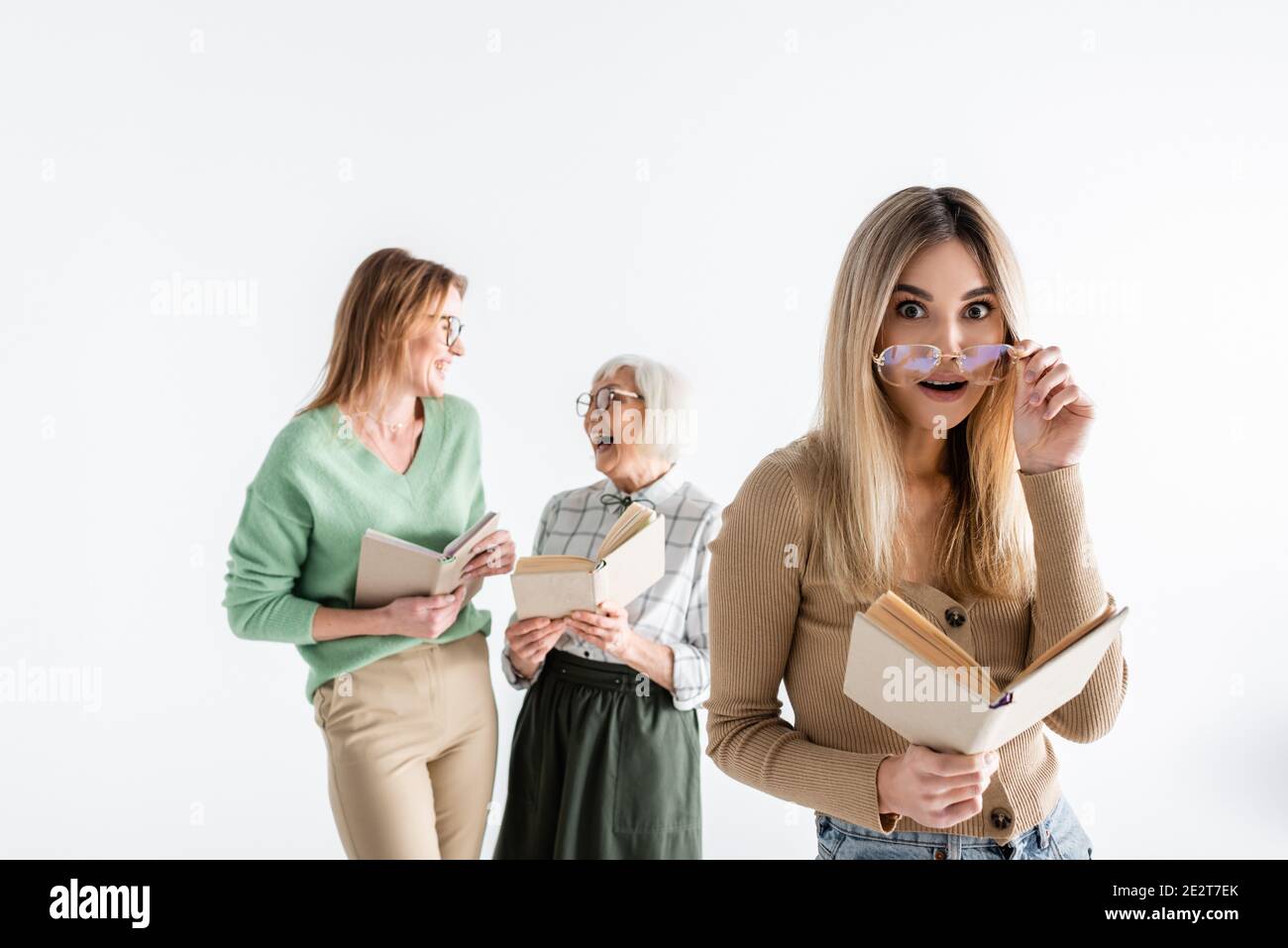 surprised woman in glasses holding book near mother and granny on blurred background isolated on white Stock Photo