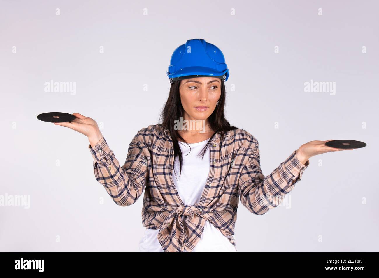 A woman in a hard hat with outstretched arms looks to the side and holds abrasive disks on a white background. Stock Photo