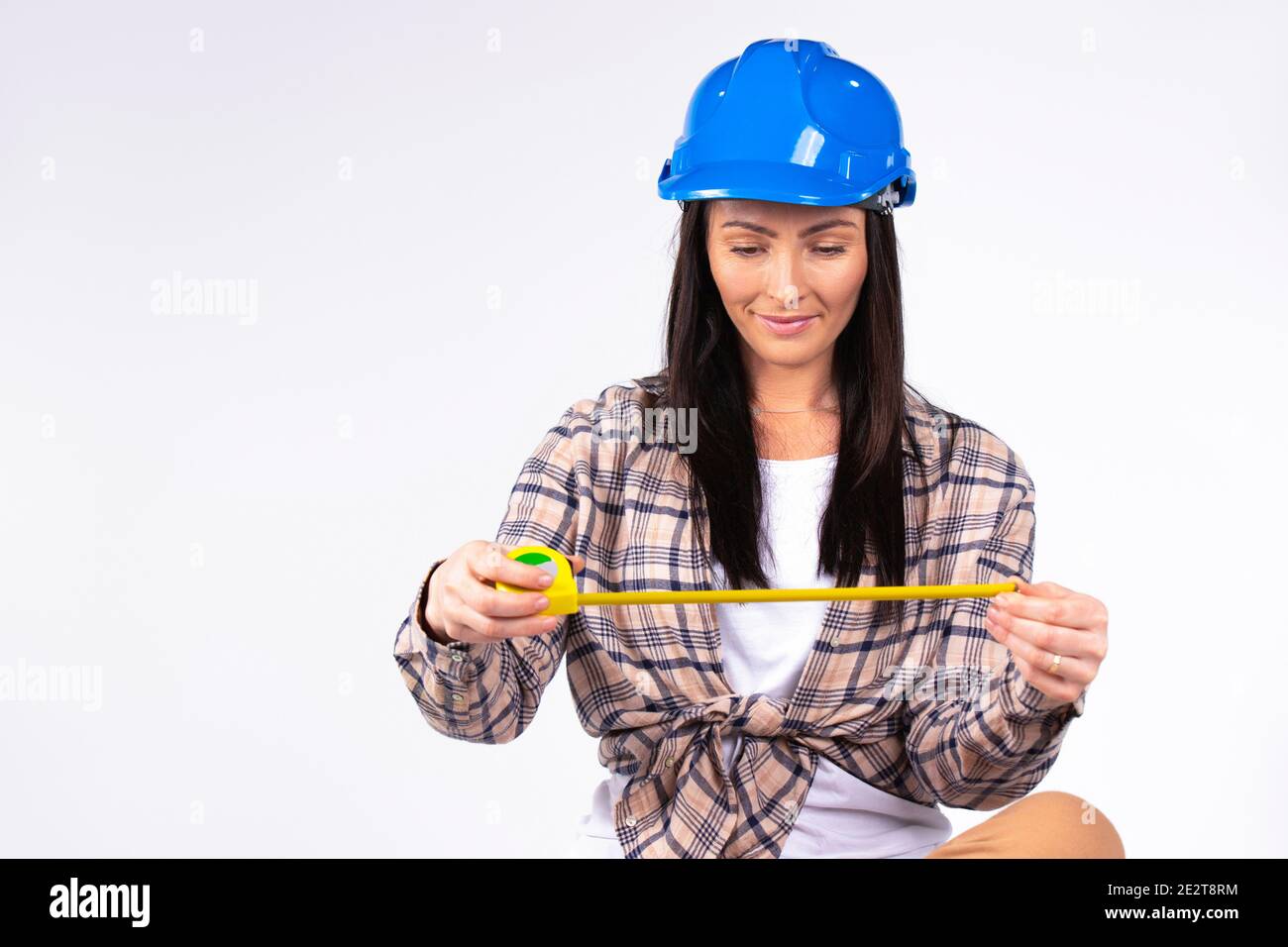Handywoman with a smile in a blue hard hat with a tape measure on a gray background with empty space for advertising. Stock Photo