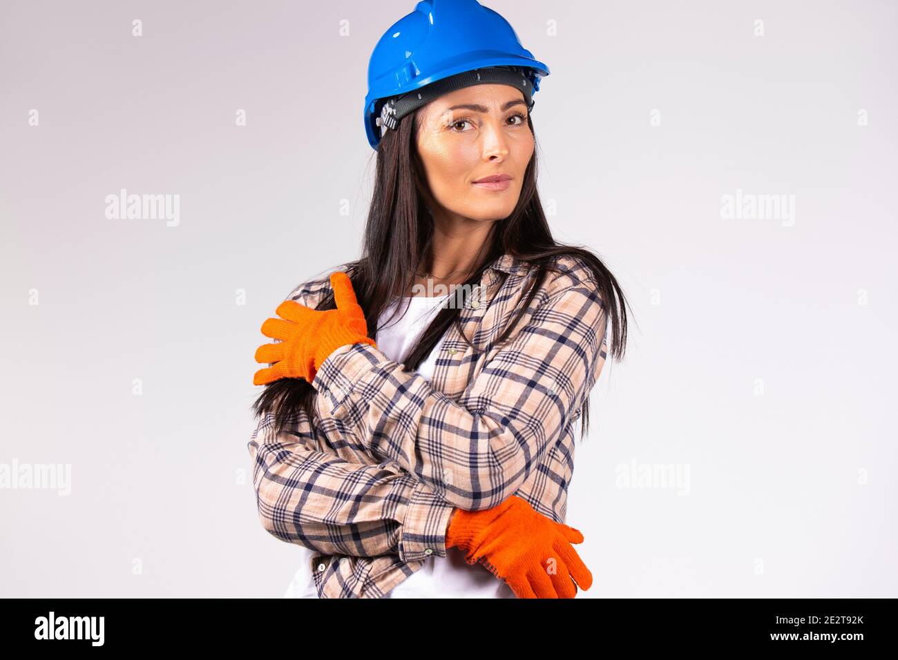Young female mechanic in hard hat and protective builder gloves posing on a gray background. Gender equality, fearless, strong . Stock Photo
