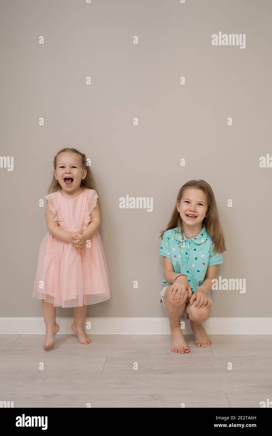 Two little sisters have fun together. Loving sisters telling secterts, smiling on beige background Stock Photo