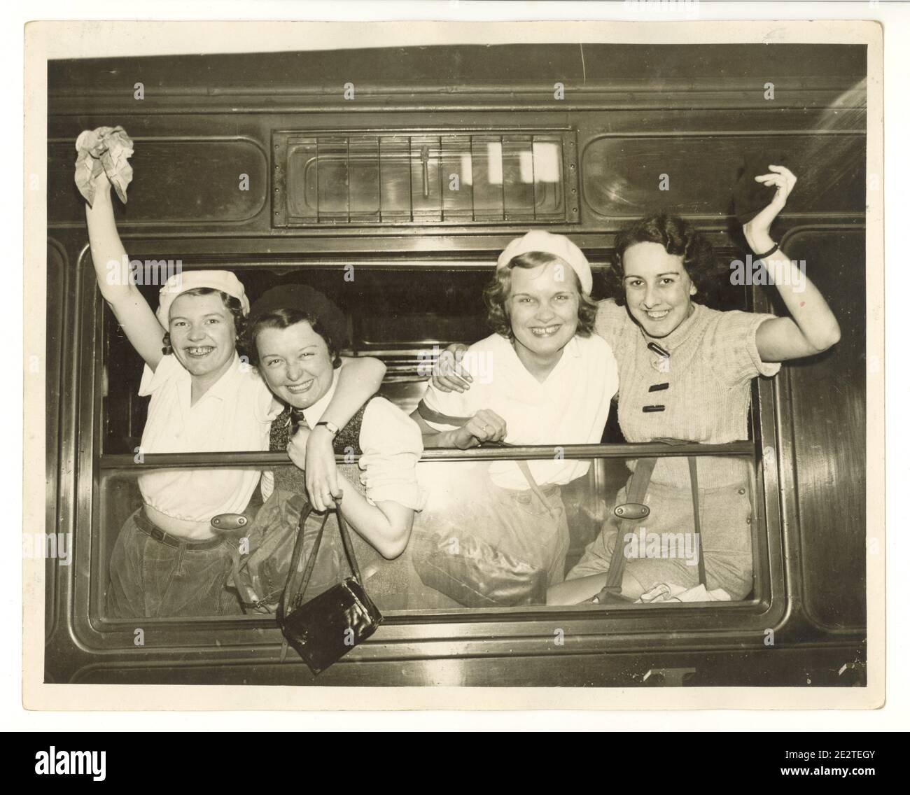 WW2 era press photo of happy young female walkers at train station, waving from a steam train window, London, U.K., 1940's Stock Photo