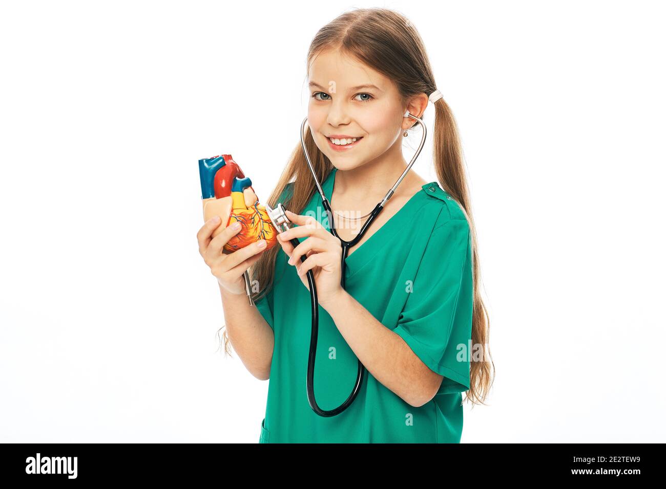 Concept of cardiac health and diagnosis of children's heart disease. Teenage girl listens to a heart model using a stethoscope Stock Photo