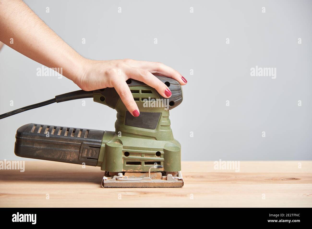 Carpentry work, hand of a young caucasian woman with her nails done sanding wood, using an electric sander. Stock Photo