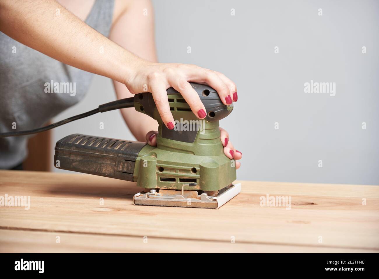 Carpentry work, detail of a young caucasian woman with her nails done sanding wood, using an electric sander. Stock Photo