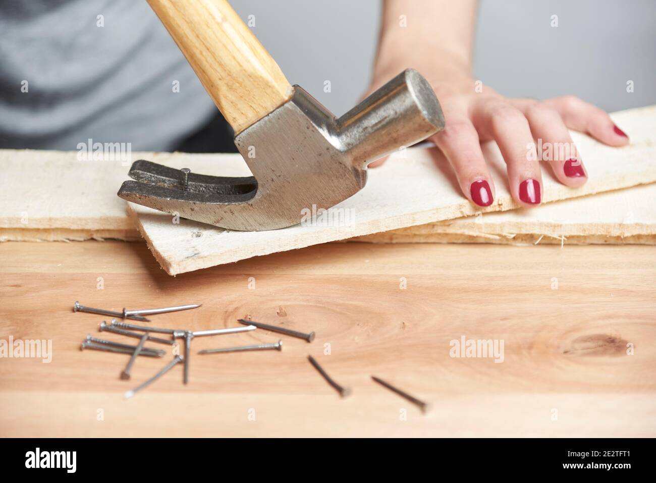 detail of carpentry a young caucasian woman with her nails done removing a nail from a piece of wood using a claw hammer 2E2TFT1