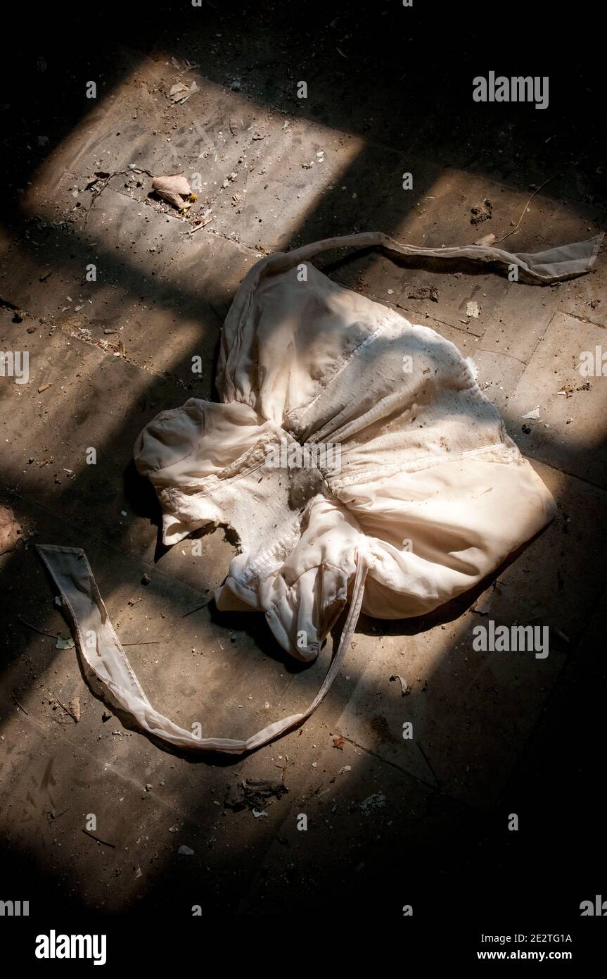 Old dirty white kids clothe on the ground with bright light entering the window. Stock Photo
