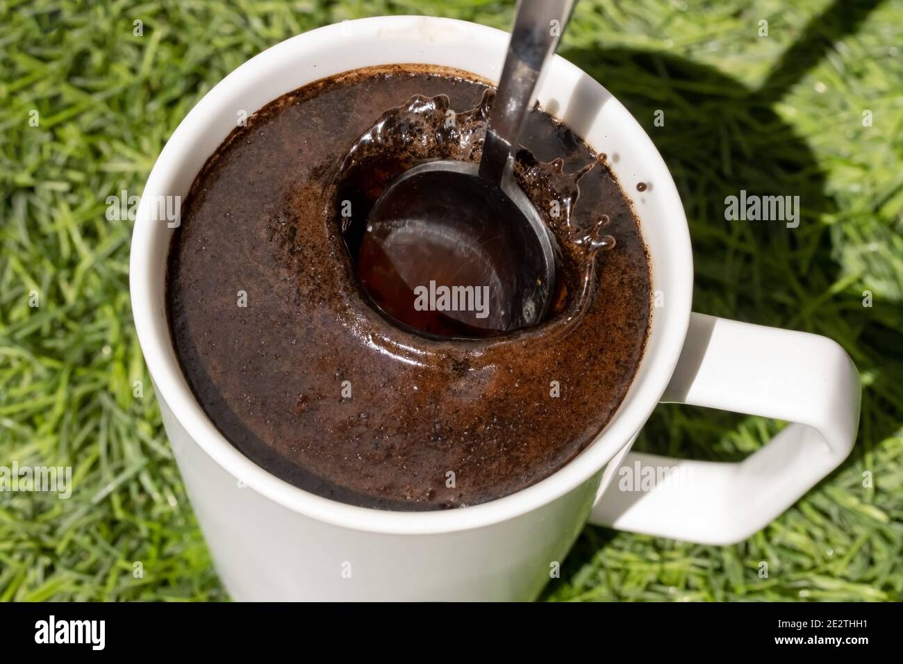A teaspoon fall down into a cup of coffee, close up view. A spoon is throw into drink. Stock Photo