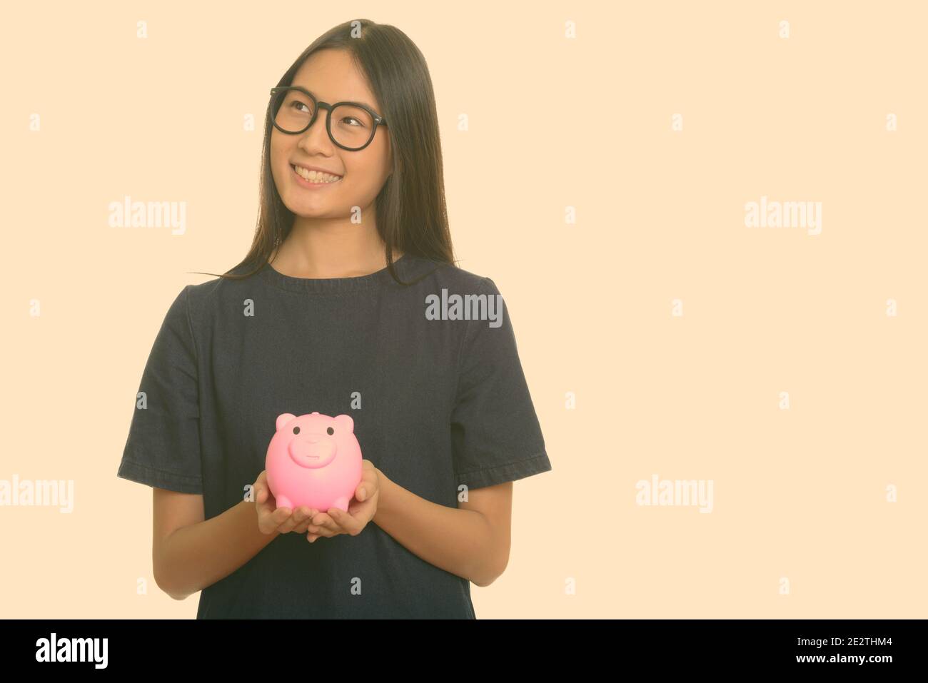 Young happy Asian teenage girl smiling and holding piggy bank while ...