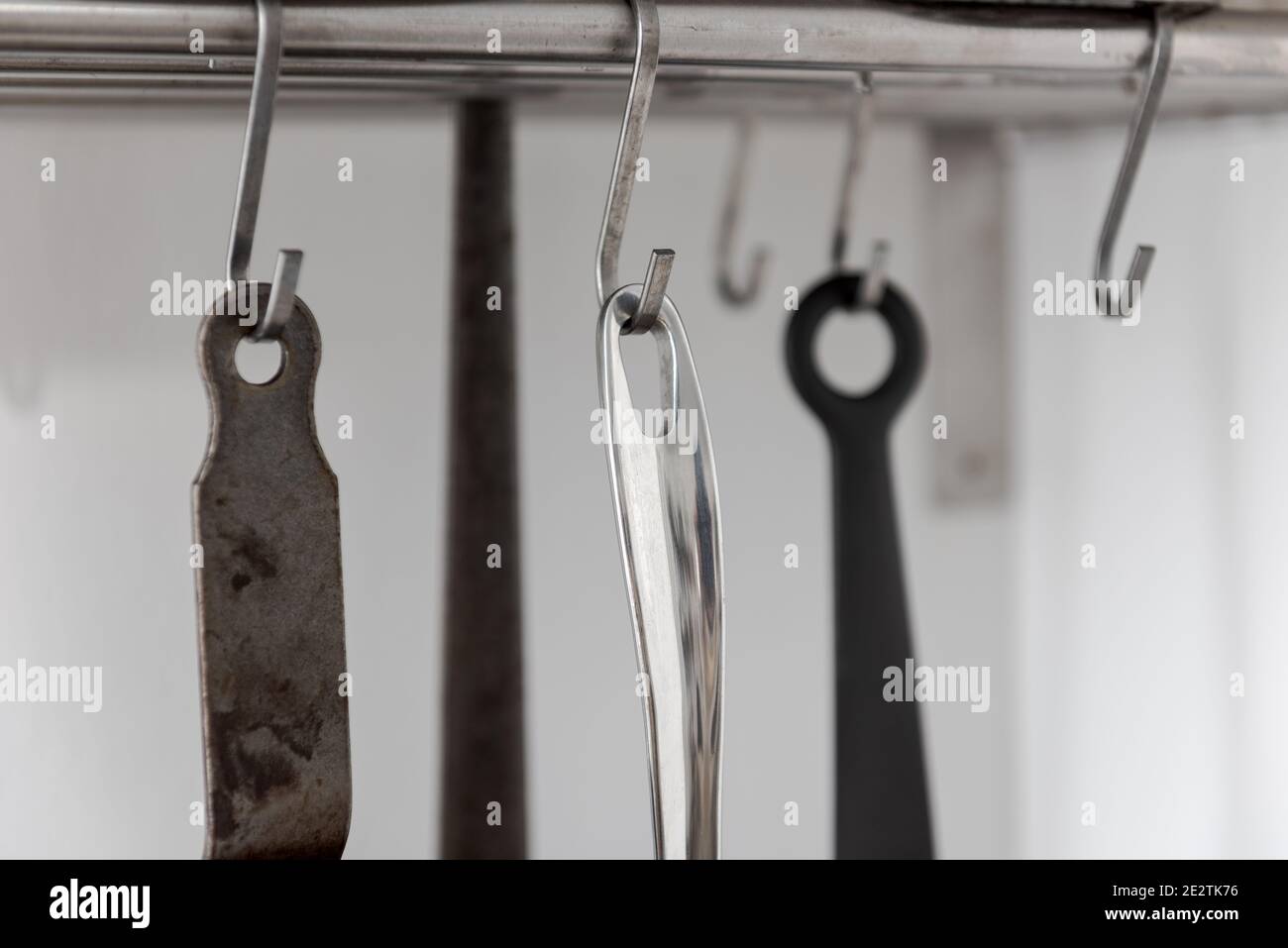 Various grips of pans in different sizes and forms for cooking and frying hanging on metal hooks from shelf in kitchen with white wall in background Stock Photo