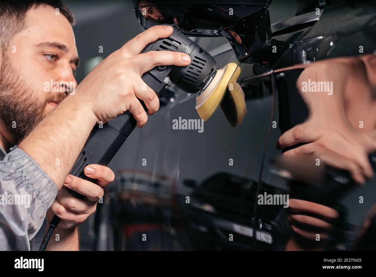 Worker polishing car with special grinder and wax from scratches at the car service station. Professional car detailing and maintenance concept Stock Photo