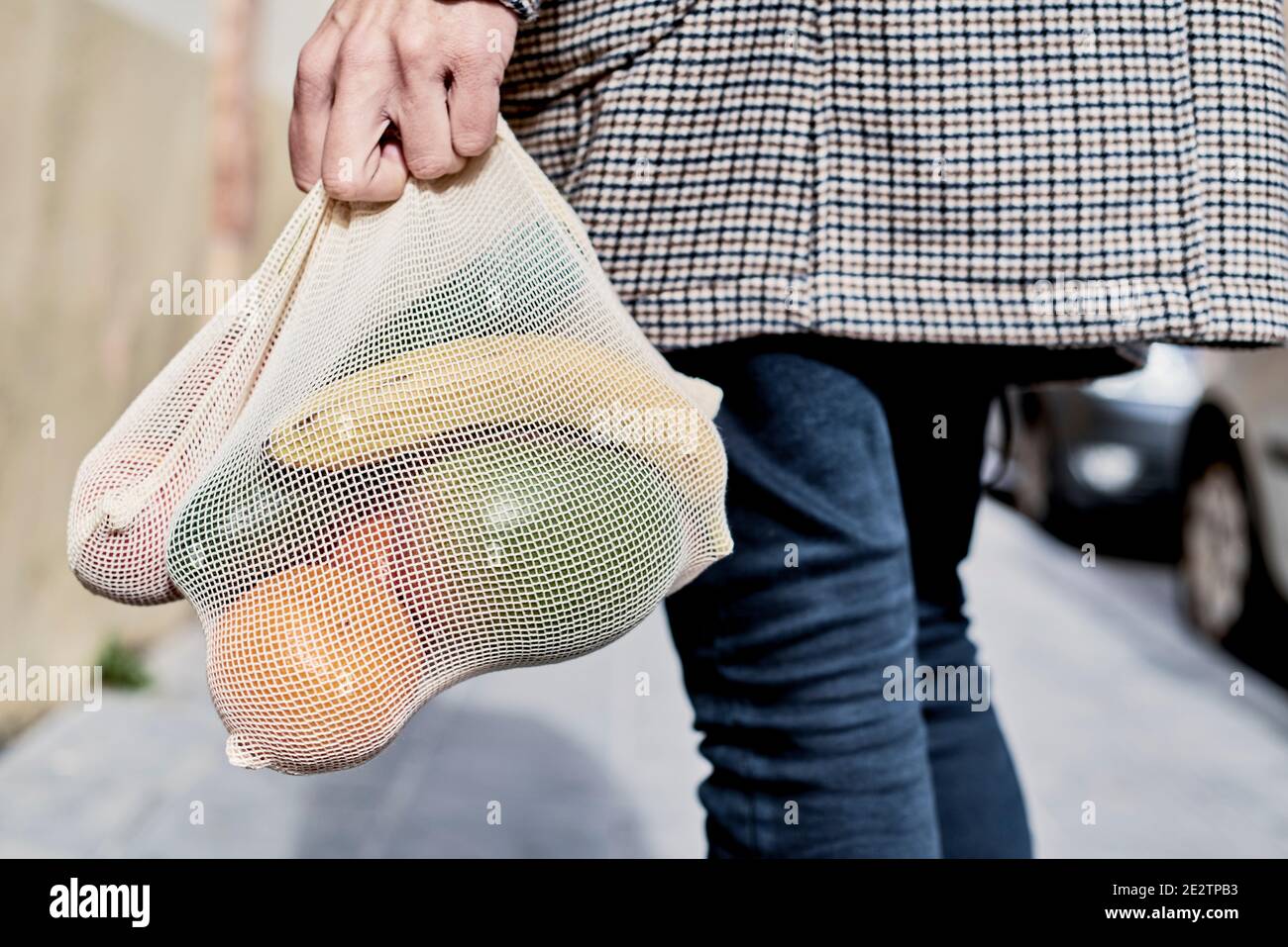 closeup of a man on the street, seen from behind, carrying a textile reusable mesh bag, used to buy groceries in bulk, full of fruit and vegs, as a me Stock Photo