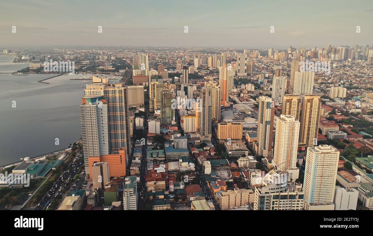Modern cityscape at ocean bay aerial. High scyscrapers and block buildings at sea coast. Traffic highway with cars, trucks. Green park at roadside. Cinematic capital town of Manila, Philippines, Asia Stock Photo