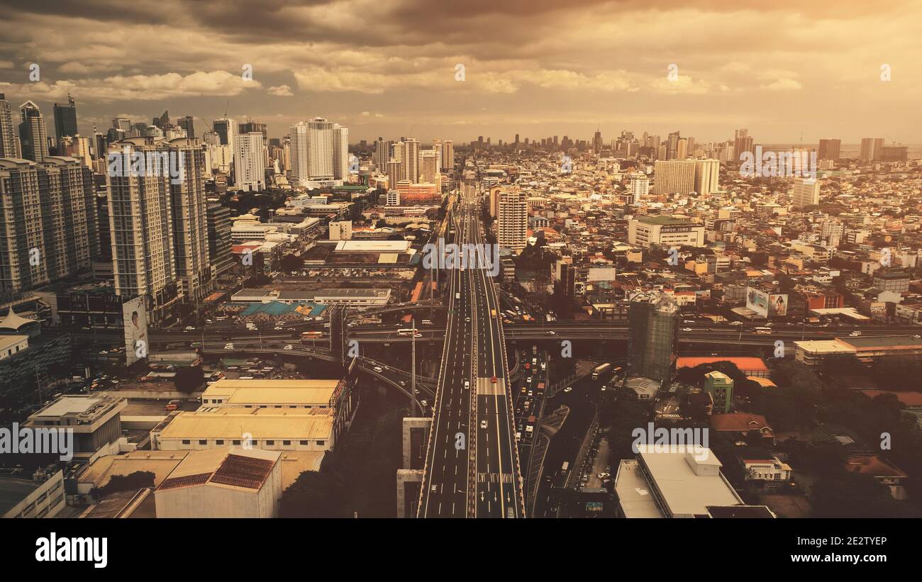 Cross bridge traffic road at sunset aerial. Modern skyscrapers buildings at downtown roadside street. Manila cityscape at sun light. Cinematic urban scenery of Philippines capital town at drone shot Stock Photo