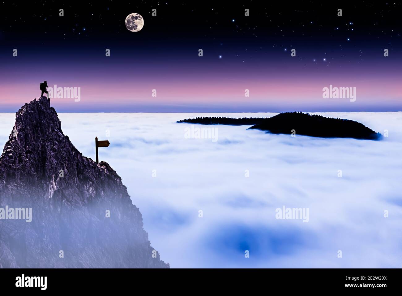 Hiker on Top of a Mountain Looking Over the Cloud Cover at Night Stock Photo