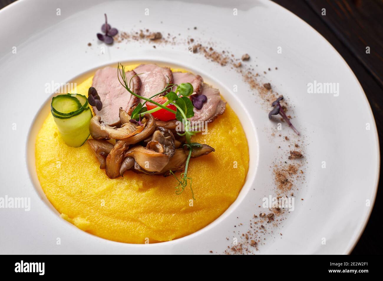 Corn porridge with meat and mushrooms, on a white plate. polenta, ugali, Banosh, mamaliga Stock Photo