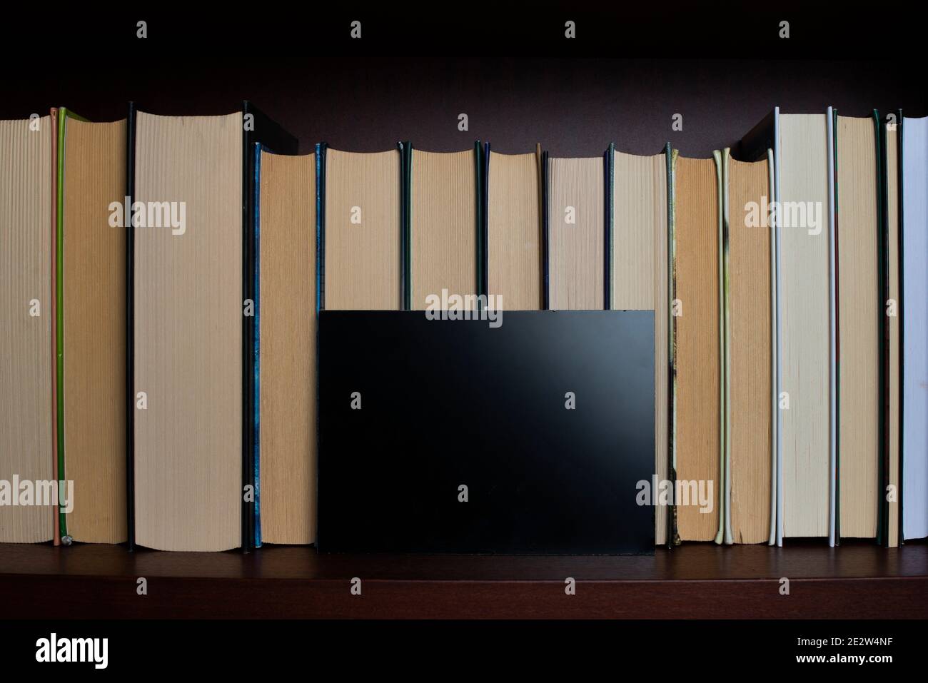 Bookshelf with books displayed backwards and piece of black glass Stock