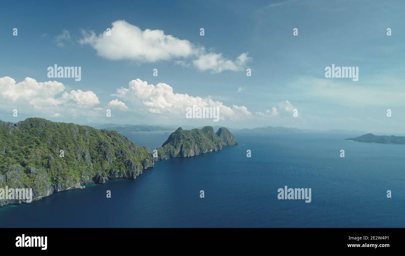 Hilly islands at blue ocean coast aerial view. Nobody nature scenery of Palawan, El Nido Isles, Philippines. Green tropic forest at mount ranges under fluffy clouds on sky. Cinematic drone shot Stock Photo