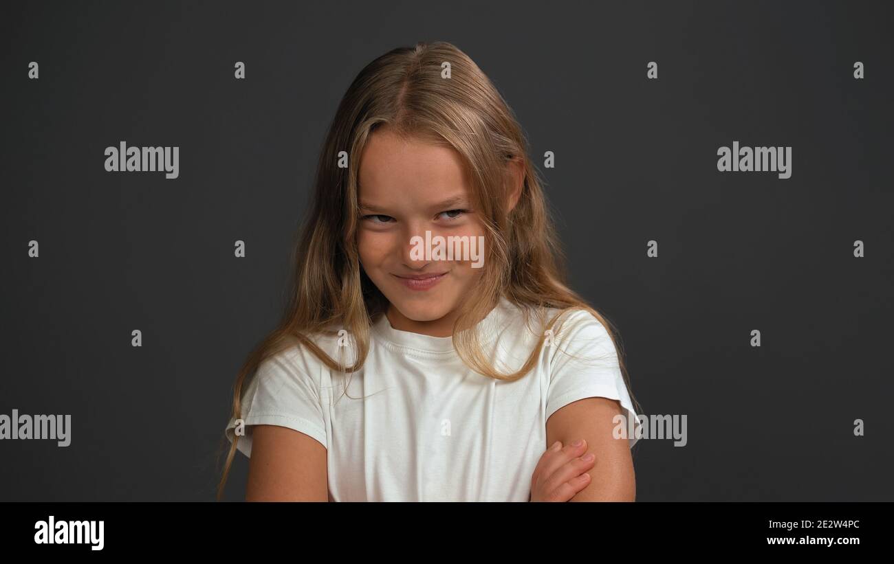 Close up. Little girl of 8,10 years with hands folded looks looks questioningly at the camera wearing white t shirt isolated on dark grey or black Stock Photo