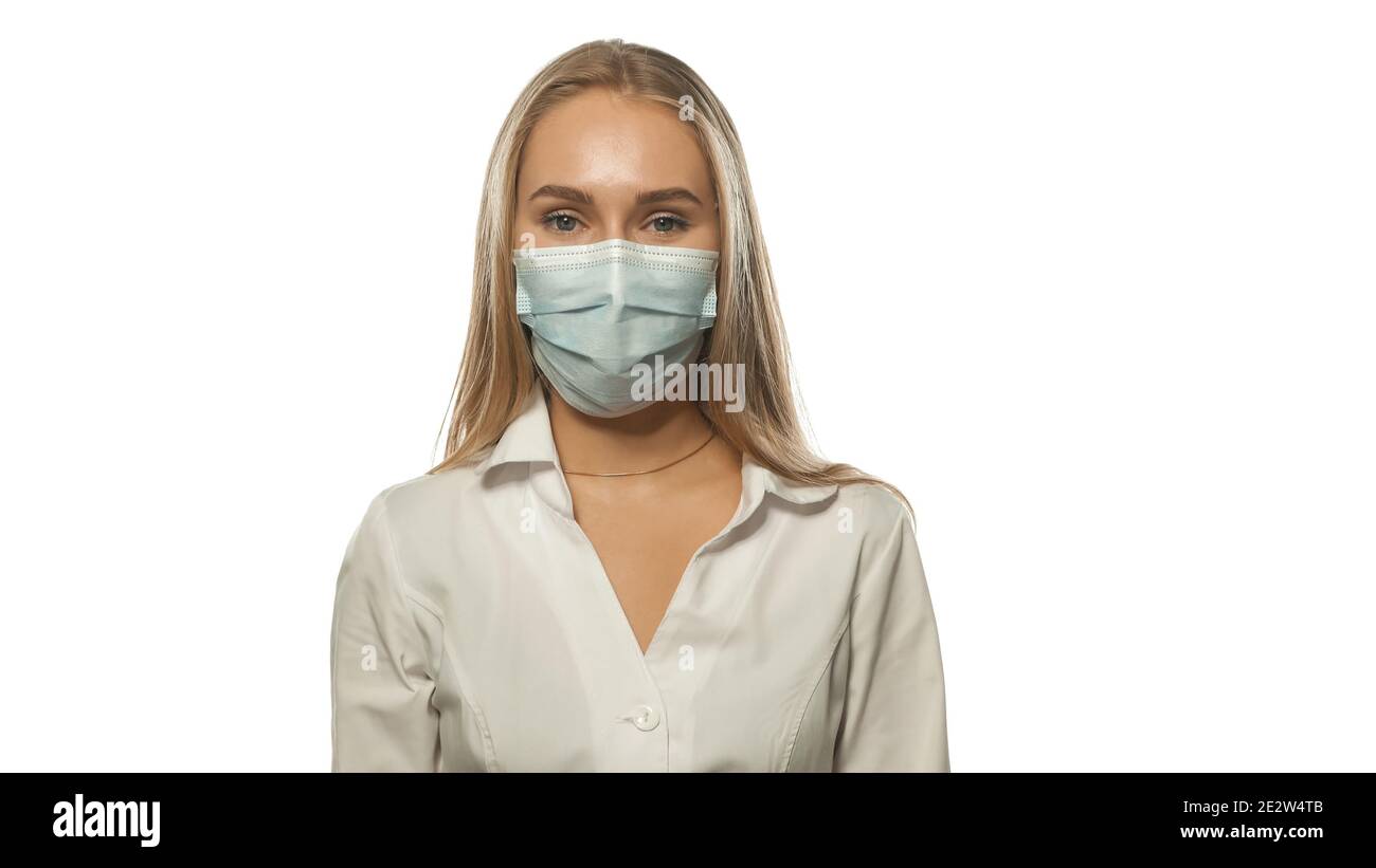 Charing blond haired nurse in a medical mask and white uniform looking at the camera. Isolated on white background Stock Photo