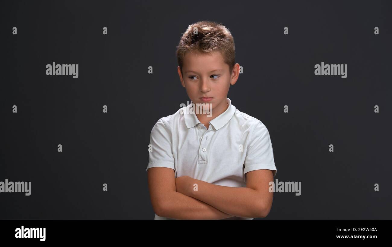 Unhappy or sad little boy looking a side frowning wearing white polo shirt and black pants isolated on black background Stock Photo