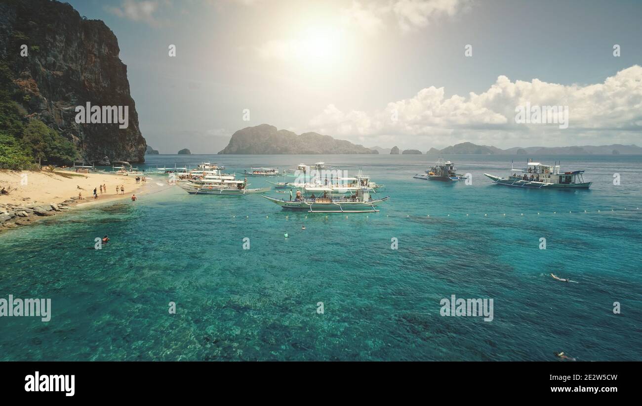 Aerial sun seascape at ocean bay azure water. Travelers at boats on tropical sea coast resort. Green forests mountain with trees at summer sunny weather. Cinematic soft sunlight drone shot Stock Photo