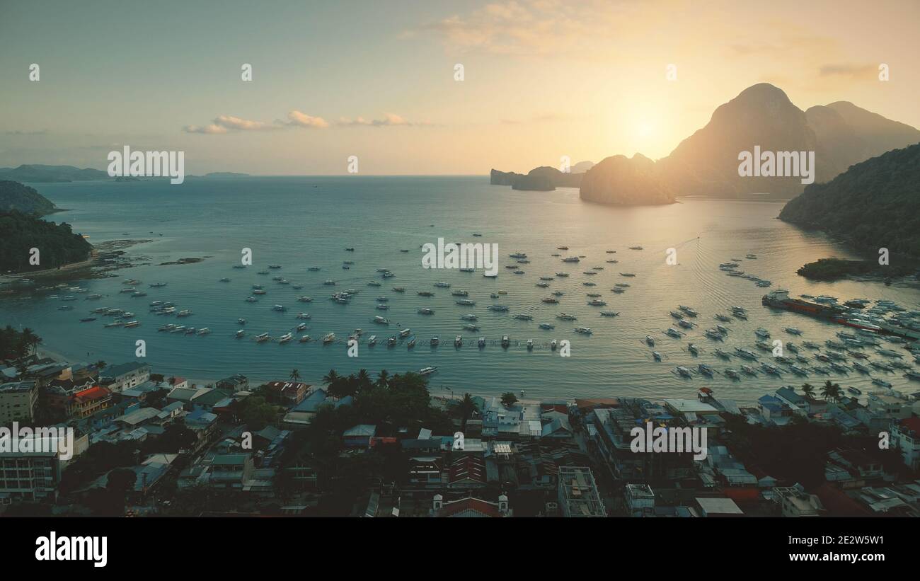 Ocean bay aerial view of sunset at port with water transport at tropical cityscape. Paradise city of Philippines islands. Greenery mount with forest trees at summer sunny day. Cinematic drone shot Stock Photo