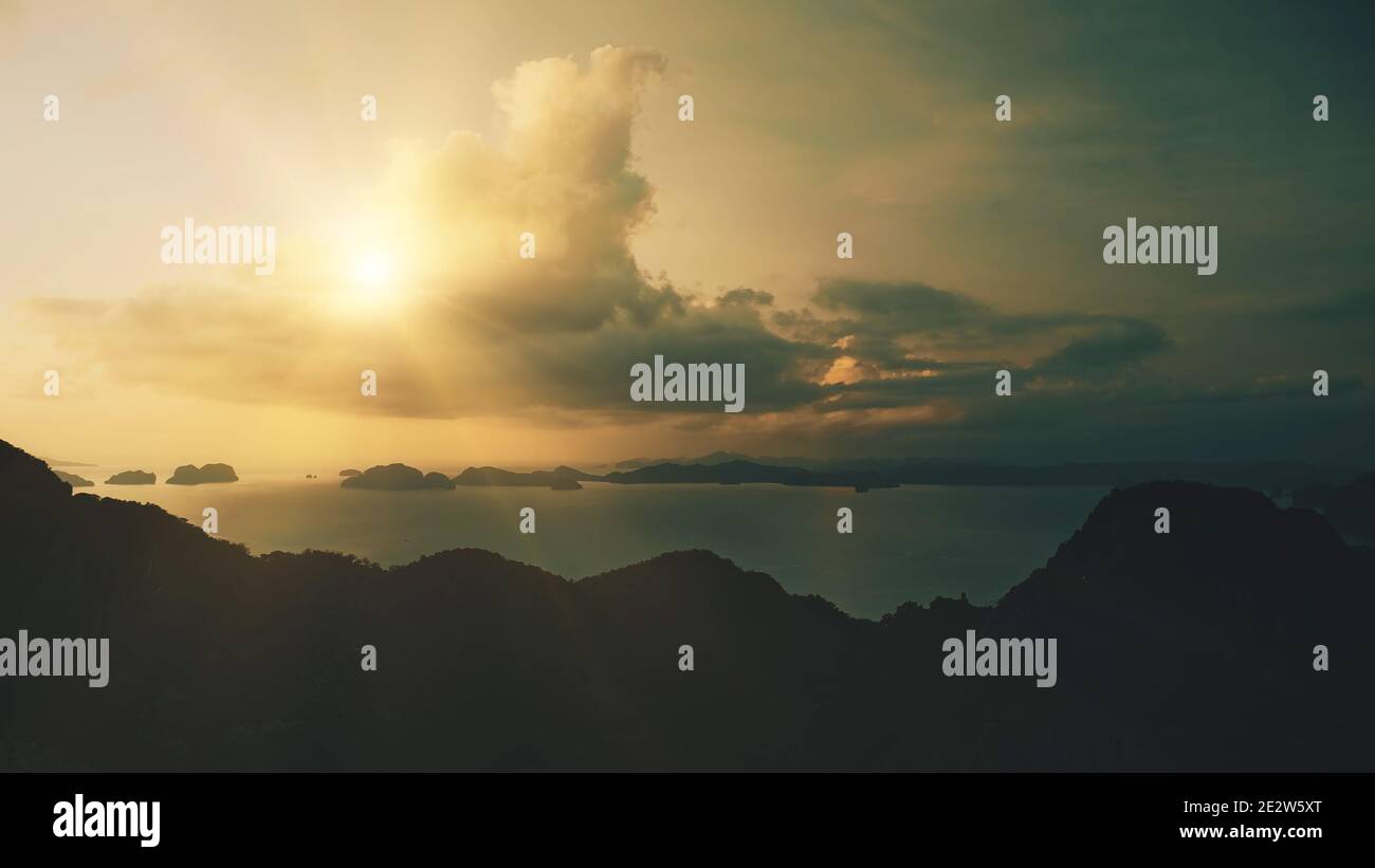 Aerial mountain island silhouette at sun shine on cloudy sky. Mounts ranges in dark tones at sun light. Epic seascape against from highlands with tropical isles. Cinematic soft shot Stock Photo