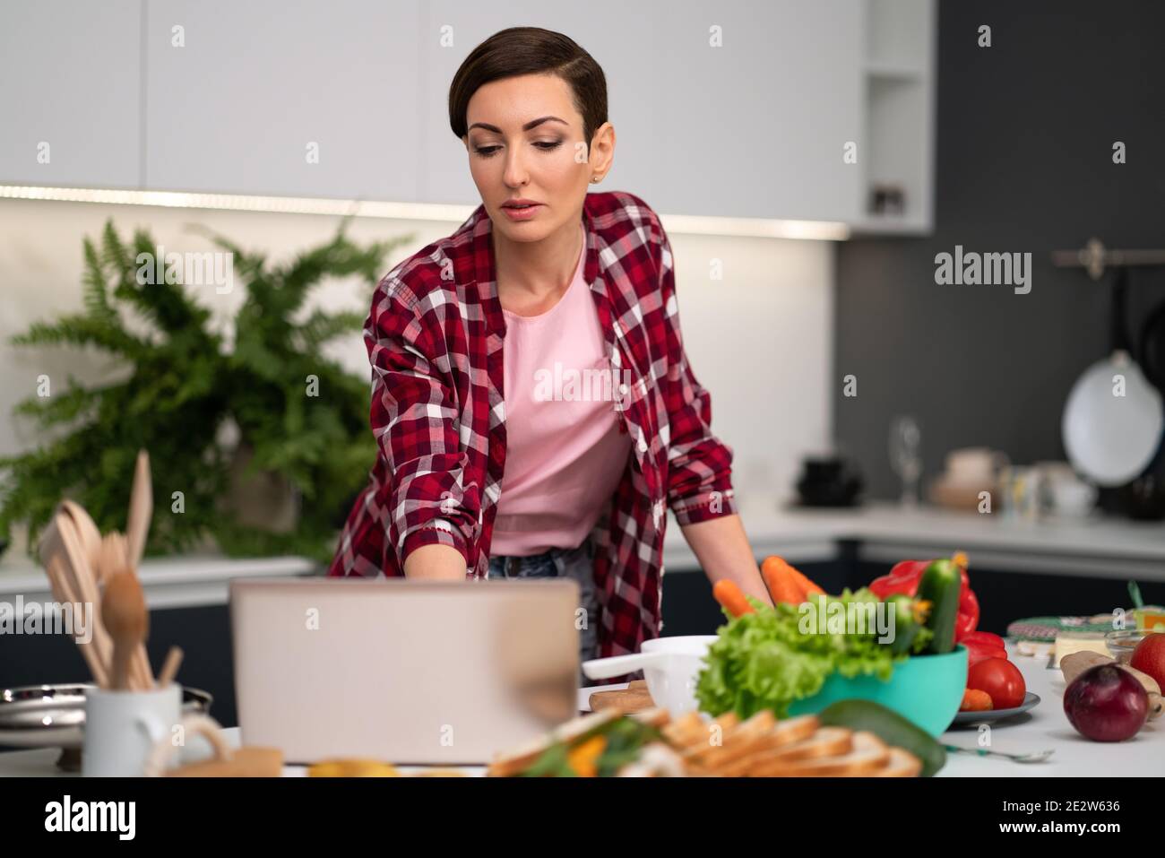 Young Woman Cooking In The Kitchen Using A Laptop Computer While Cooking Young Housewife Searching Online Recipes Or Watching Online Tv Show While Stock Photo Alamy