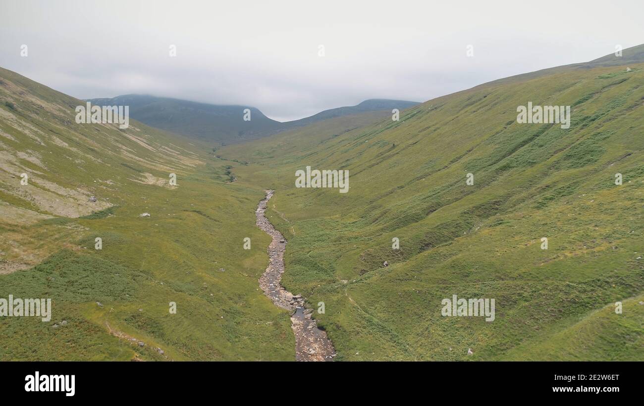 Green mountains path aerial. Narrow way from hill to cloudy peak. Cinematic nobody nature landscape of Arran Island, Scotland. Rock mount stream river banks. Summer vacation at greenery ranges Stock Photo