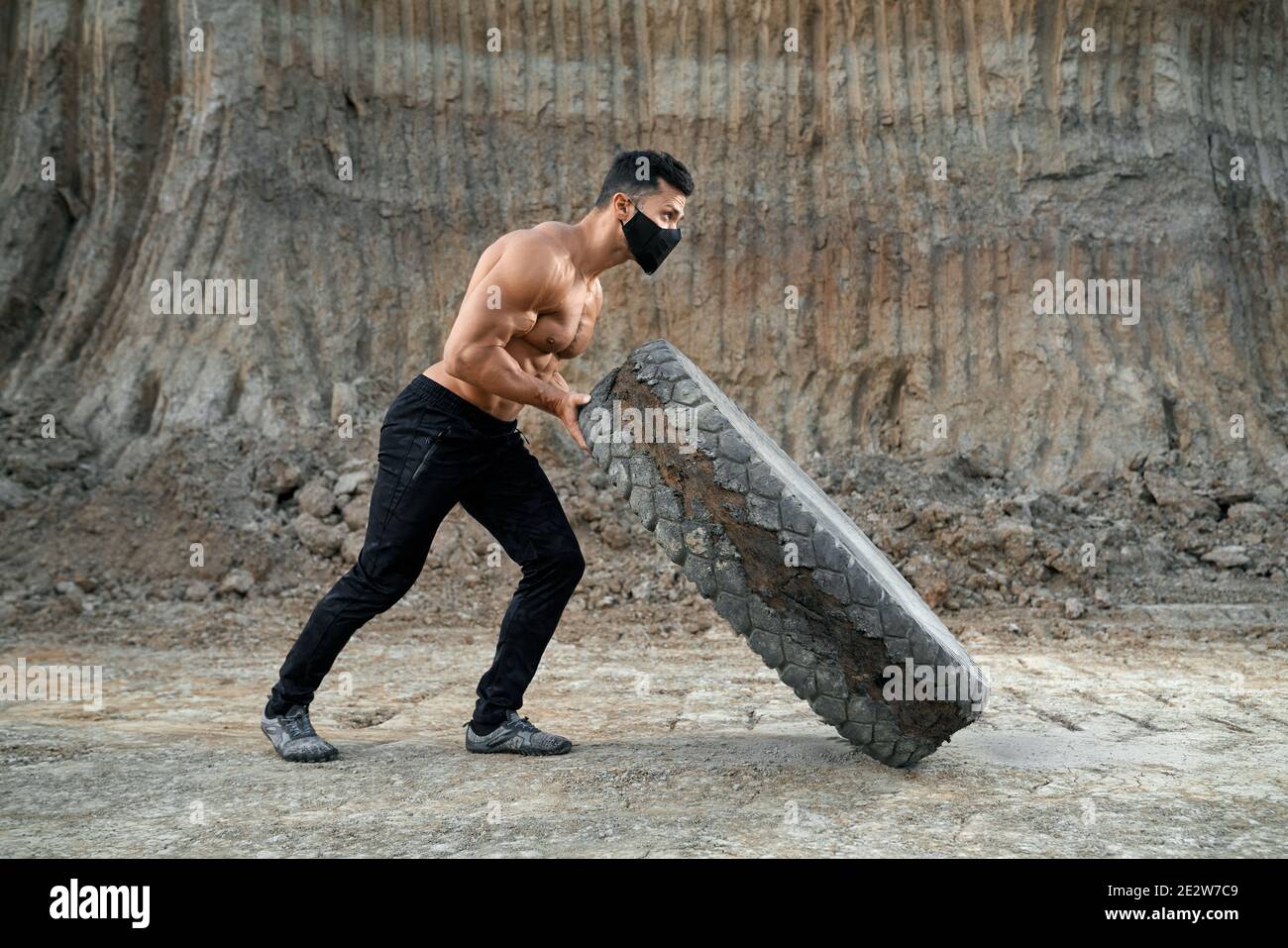 Side view of muscular man with bare torso workout with large heavy wheel at sand pit. Strong active guy wearing sport pants and protective face mask Stock Photo Alamy