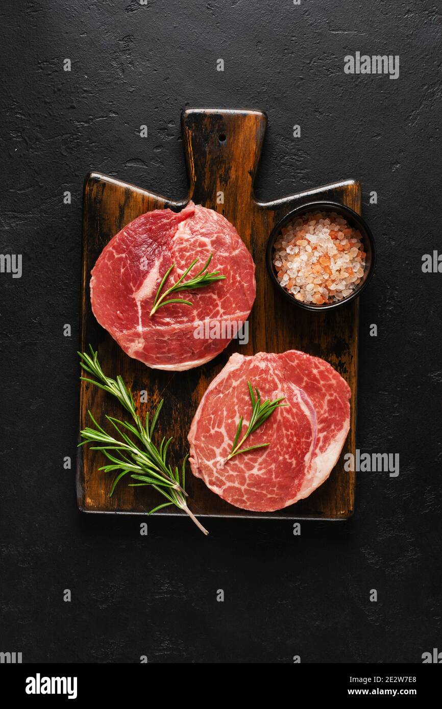 Two fresh Parisienne raw steak on wooden Board with salt, pepper and rosmary in a rustic style on old wooden background. Black angus. Top view. Stock Photo