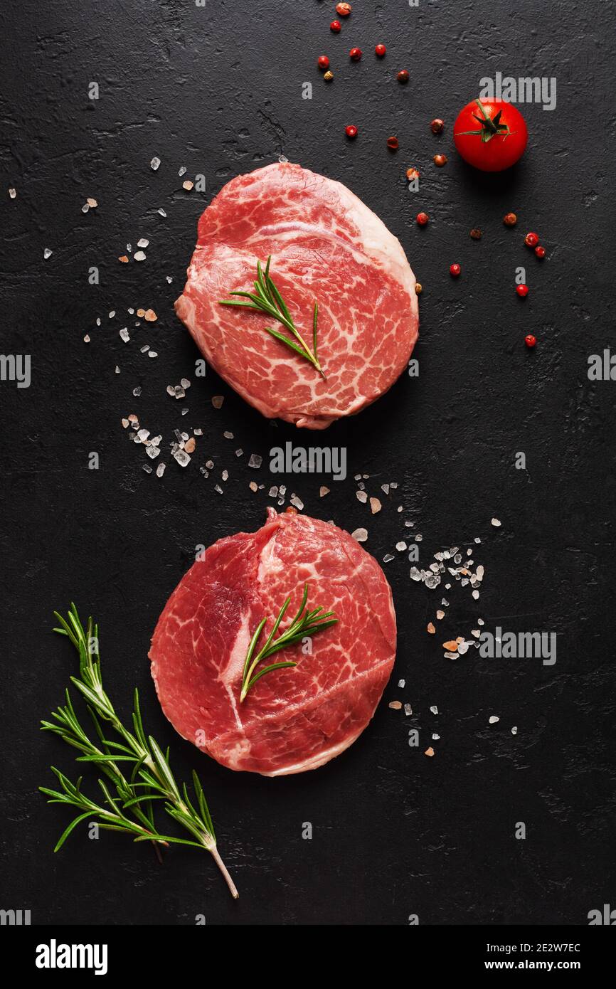 Two fresh Parisienne raw steak on white parchment paper with salt, pepper and rosmary in a rustic style on old stone background. Black angus. Top view Stock Photo