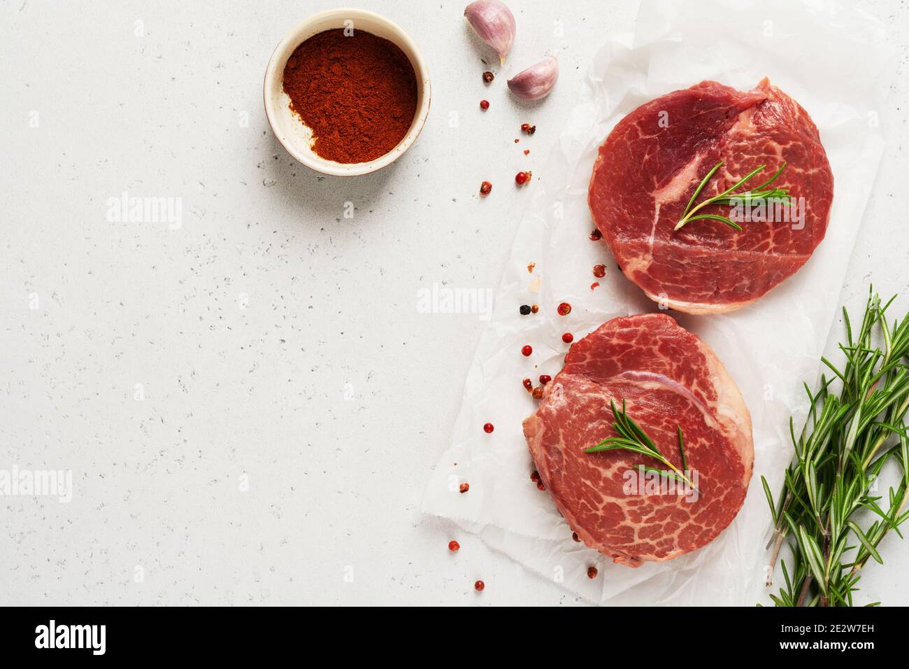Two fresh Parisienne raw steak on white parchment paper with salt, pepper and rosmary in a rustic style on old wooden background. Black angus. Top vie Stock Photo