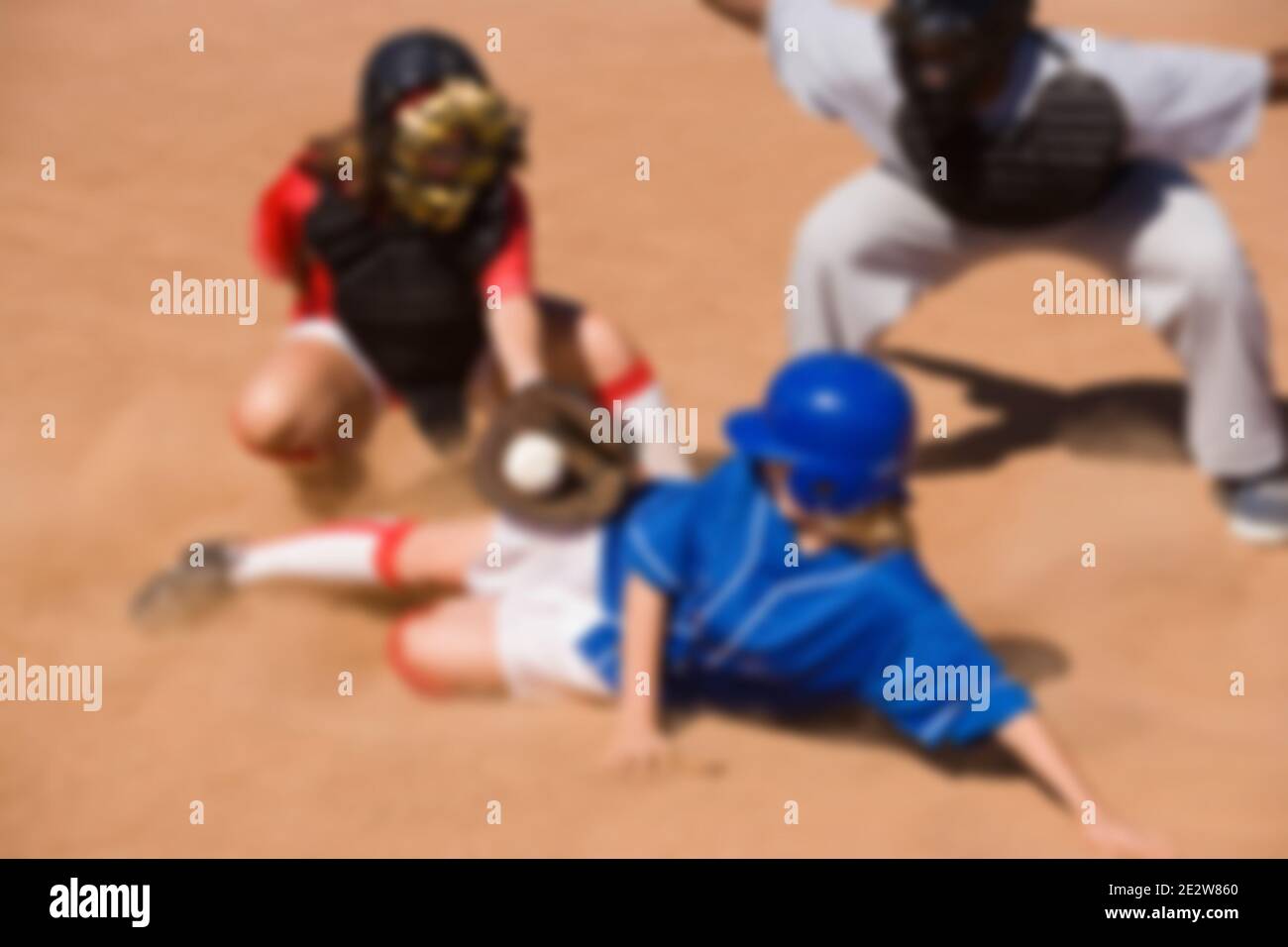 Softball player sliding into home plate while umpire rules safe Stock Photo