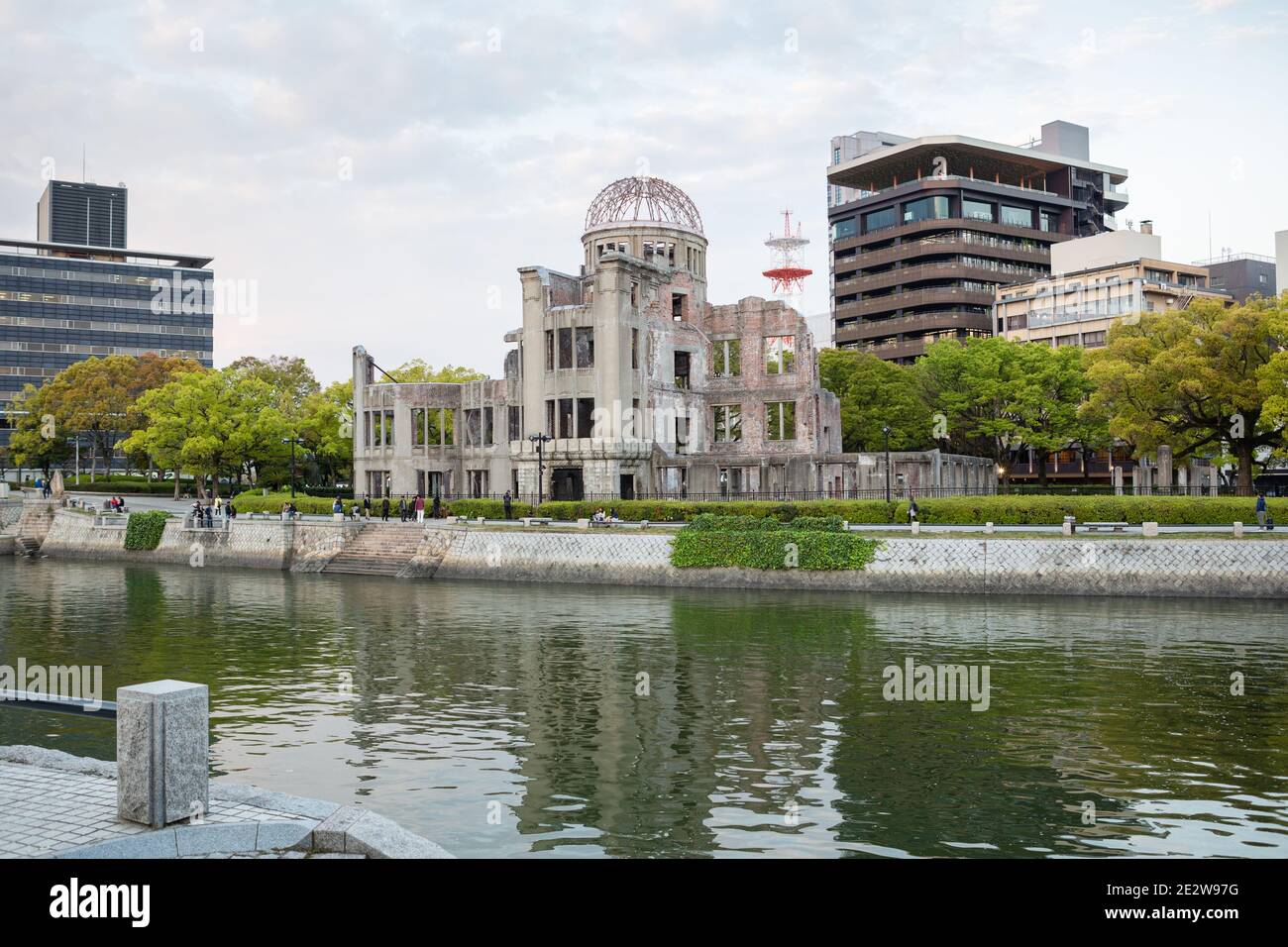 Hiroshima Peace Memorial, viewed across and reflected in the river, with the city behind and people walking past, Hiroshima, Japan Stock Photo