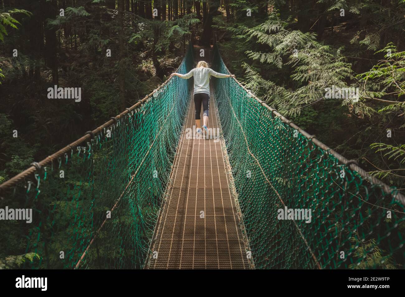 A young woman crosses a forest suspension bridge on the Juan de Fuca