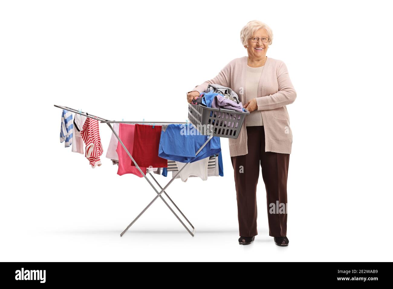 Elderly woman holding a laundry basket with clothes next to a clothing line rack isolated on white background Stock Photo