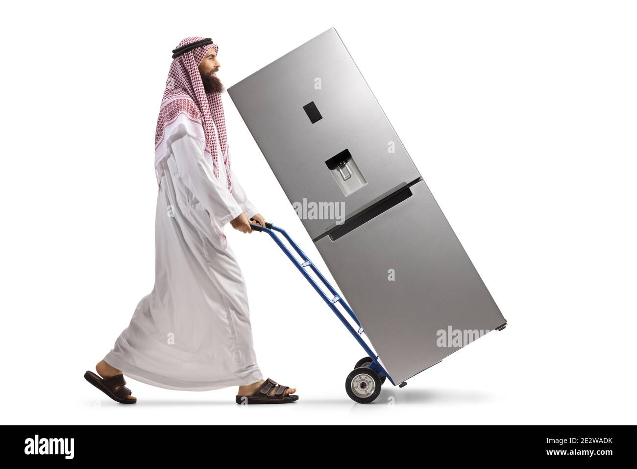 Full length profile shot of a saudi arab man pushing a hand truck with a fridge isolated on white background Stock Photo
