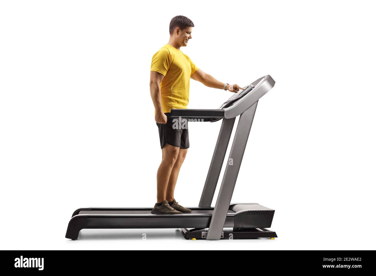 Full length profile shot of a young man pushing a button on a treadmill isolated on white background Stock Photo