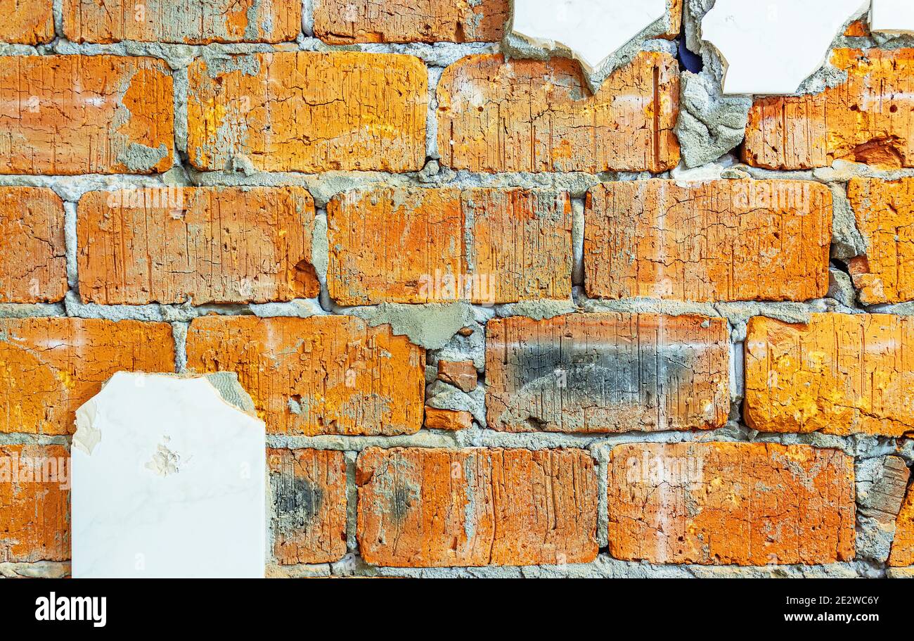 Textured background of old cracked red brick with the remains of unbroken tiles. Internal repair of premises, apartments. Removal of ceramic tiles and Stock Photo