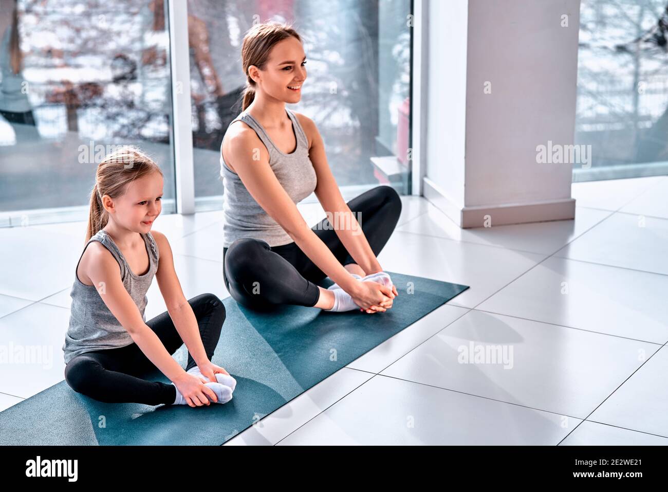 High angle view of two beautiful blond haired girls practicing butterfly  pose. Mom and daughter meditate while sitting on yoga mat in health club.  Pil Stock Photo - Alamy