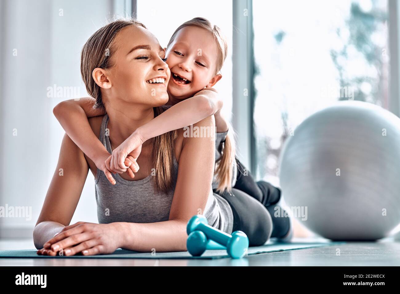 Portrait of happy laughing little girl lying on mom's back while resting after training in fitness club. Welness concept Stock Photo