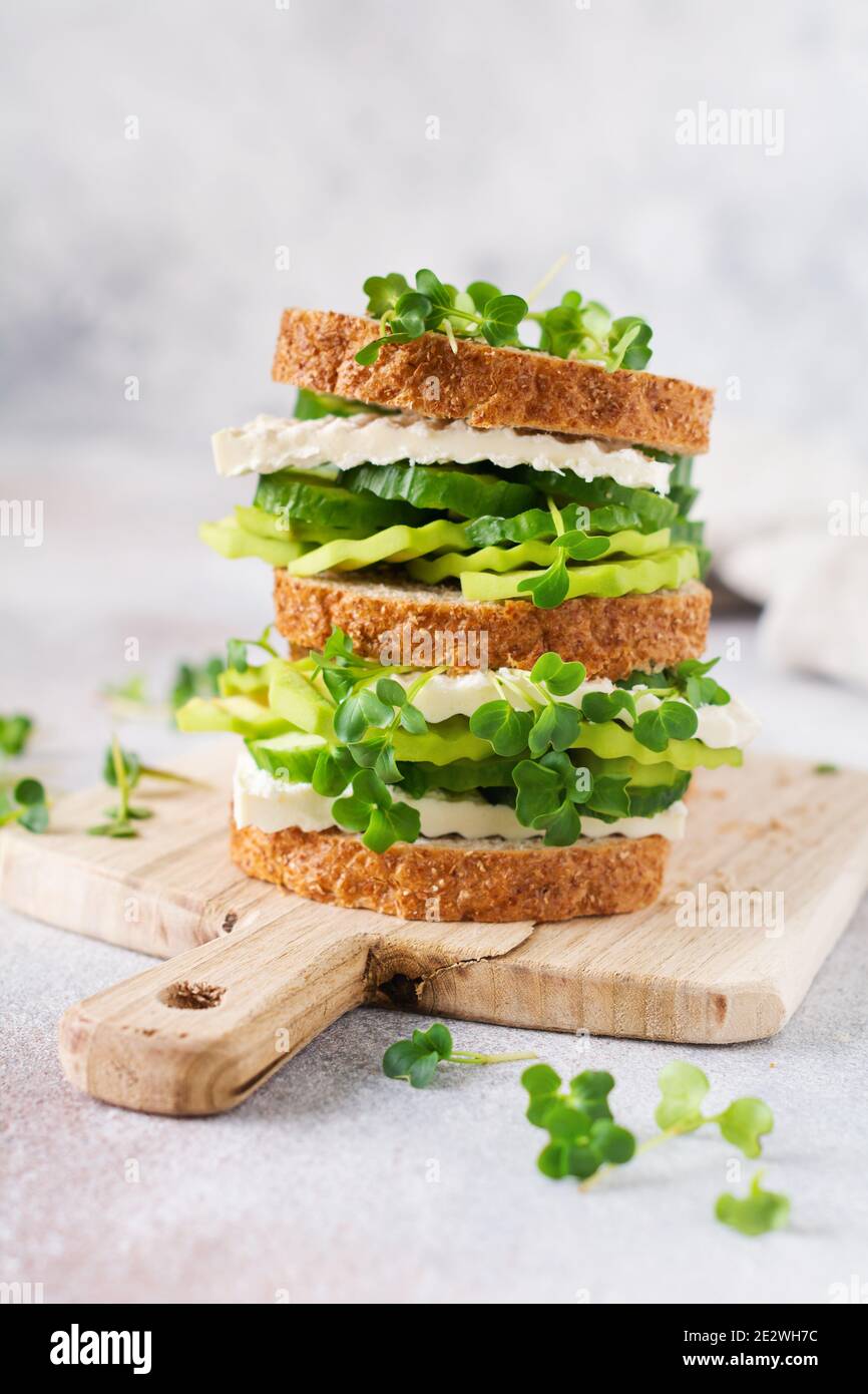 Avocado, cucumber and feta cheese sandwich decorated with micro-greens and multi-grain bread on a simple wooden stand for a healthy breakfast. Selecti Stock Photo